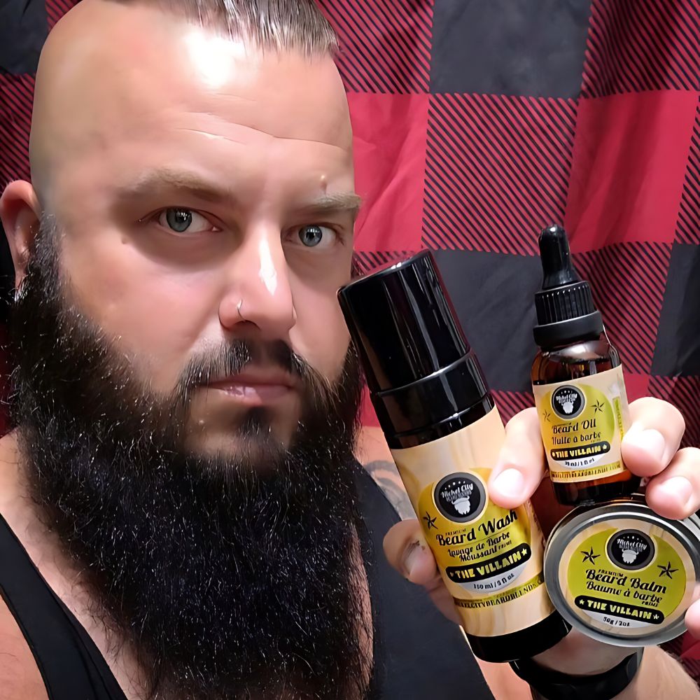 Bearded man holding Nickel City Beard Blends Professor Trinity Bundle – beard oil, balm and wash – in front of red and black plaid backdrop.