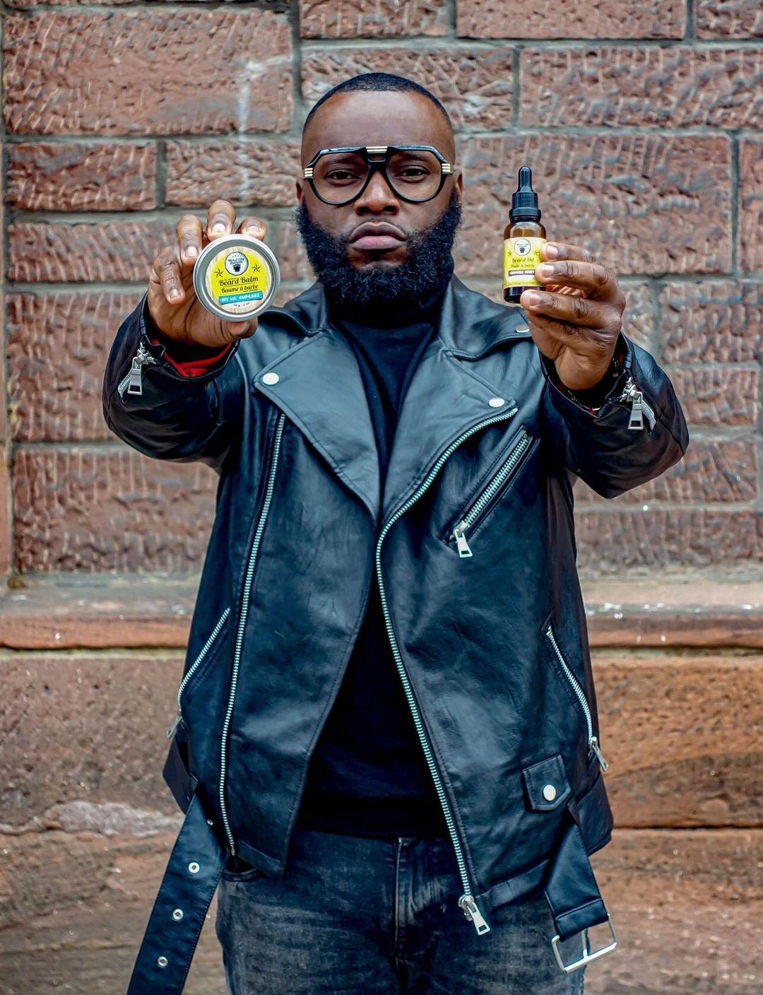 Man holding two beard products against a brick wall