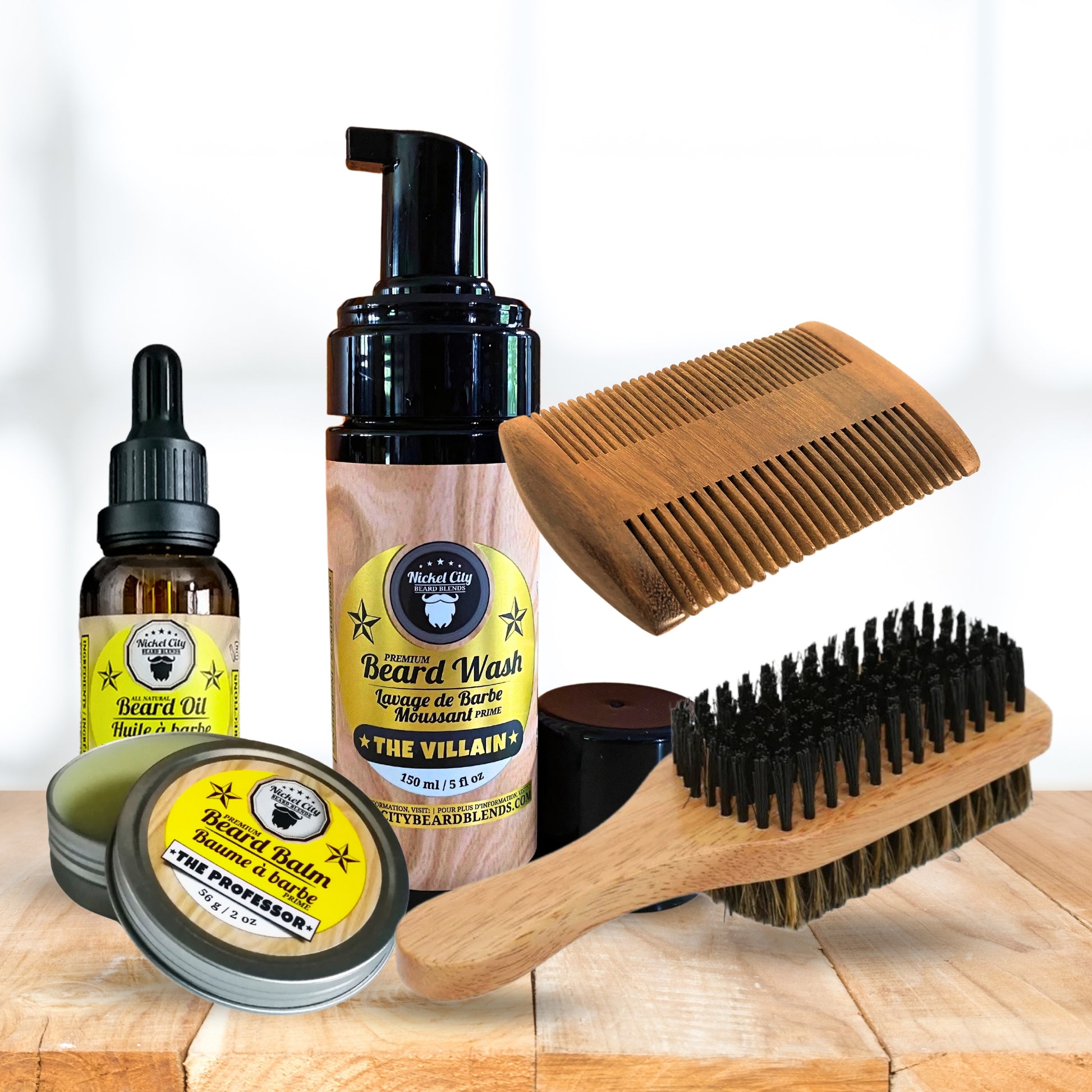 Collection of beard care products including oil, wash (shampoo), balm, comb and brush on a wooden surface with a white background.
